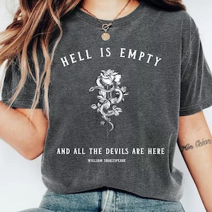May include: Dark gray t-shirt with the quote "Hell is Empty and All the Devils are Here" and a floral snake graphic. The text is in white, and the design includes a rose and a snake.