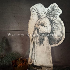 Könnte beinhalten: Ein sepiafarbener Papierausschnitt des Weihnachtsmanns im Profil, der einen Kapuzenmantel trägt und einen großen Sack voller Tannenzweige trägt. Der Text WALNUT RIDGE PRIMITIVES und 10 INCH PAPER SEPIA SANTA PRINTABLE GRAPHIC WITH BASIC INSTRUCTIONS ist sichtbar.
