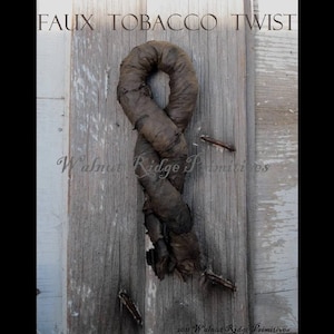 May include: A faux tobacco twist, a decorative item, is displayed against a weathered wooden background. The twist is a dark brown color, and the text "FAUX TOBACCO TWIST" is at the top. The words "Walnut Ridge Primitives" are also visible.
