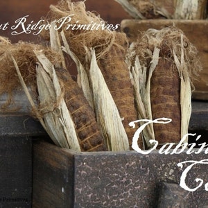 May include: Dried corn husks in a wooden box with the text "Walnut Ridge Primitives" and "Cabin Corn".