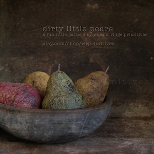 Op de afbeelding: Een rustieke houten kom gevuld met vier peren, één paarse, één bruine en twee groene. De peren zijn in een tros gerangschikt, met de paarse peer vooraan. De kom staat op een donkerbruin oppervlak. De tekst "dirty little pears" is in wit op een donkerbruine achtergrond boven de kom geschreven. De tekst "a fun little pattern by walnut ridge primitives" is in wit op een donkerbruine achtergrond onder de kom geschreven. De tekst "etsy.com/shop/wrprimitives" is in wit op een donkerbruine achtergrond onder de kom geschreven.