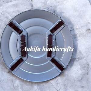May include: A silver shield with brown leather straps and buckles. The shield has a circular design with a ridged centre. The text "Aakifa handicrafts" is printed on the shield.