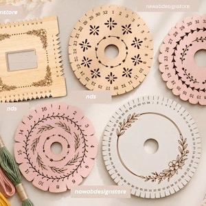 Op de afbeelding: Een verzameling houten borduurgaren-organizers, waaronder één vierkant bord met bloemengravures en vier ronde borden met genummerde randen en decoratieve patronen, vergezeld door verschillende strengen borduurgaren.