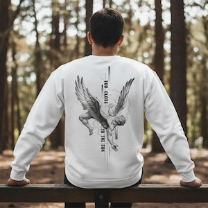 Puede incluir: Sudadera blanca con un gráfico en blanco y negro de una figura cayendo con alas. El texto "TOO CLOSE TO THE SUN" está impreso verticalmente en la parte posterior. La sudadera es de manga larga y tiene cuello redondo.