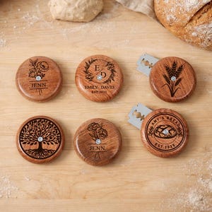 May include: Six round wooden bread lame handles with engraved designs and text. The handles feature floral, wheat, and tree motifs, along with the names "JENN" and "AMY'S BREAD" and the text "EST.2025" and "EMILY DAVID EST.2025".