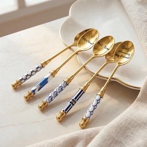 May include: Set of four gold-colored spoons with decorative handles. Each spoon has a different blue and white patterned handle. The spoon bowls have the phrases "Coffee time!", "Best teas", and "Good Morning my friend!" printed on them.