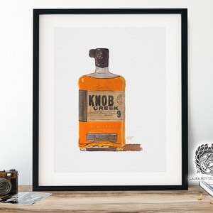 May include: A framed print of a bottle of Knob Creek whiskey. The bottle is amber-colored with a dark brown cap and a label that reads "Knob Creek" and "9". The artwork is set against a white background.