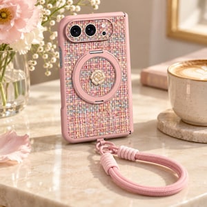 May include: A pink phone case with a textured, multi-colored tweed fabric inlay. The case features a circular magnetic ring on the back with a small white rose emblem in the center and a matching pink braided wrist strap attached to the bottom.