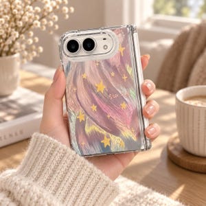 K&ouml;nnte beinhalten: Eine transparente Handyh&uuml;lle f&uuml;r ein faltbares Ger&auml;t mit einem abstrakten Pinselstrich-Design in Rosa-, Lila- und Blaut&ouml;nen, verziert mit gelben Sternen und dem Schriftzug Star light in einer feinen wei&szlig;en Schreibschrift.
