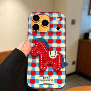 May include: Clear phone case with a red, white, and blue checkered pattern and a red horse applique. The case has a rectangular shape and features the text "BKDD" at the bottom.