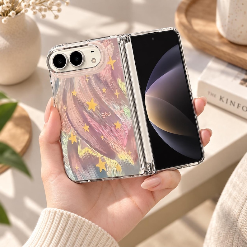 K&ouml;nnte beinhalten: Eine faltbare Smartphone-H&uuml;lle mit transparenter R&uuml;ckseite, die ein abstraktes, mehrfarbiges Pinselstrichmuster in Rosa-, Blau- und Gelbt&ouml;nen aufweist, akzentuiert durch kleine goldene Sterne und den Schriftzug Star Light auf der Oberfl&auml;che.