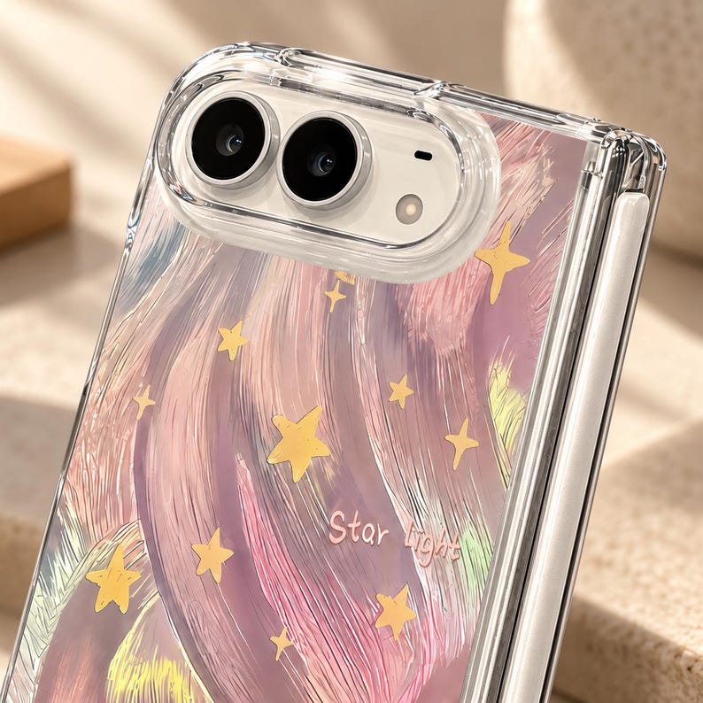 K&ouml;nnte beinhalten: Eine transparente Handyh&uuml;lle f&uuml;r ein faltbares Ger&auml;t mit einem gemalten Design aus wirbelnden rosa, violetten und gelben Pinselstrichen mit verstreuten gelben Sternen. Der Text "Star Light" ist in hellrosa Schreibschrift aufgedruckt.