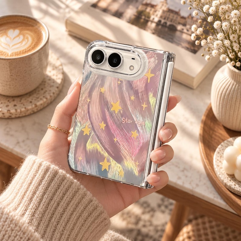 K&ouml;nnte beinhalten: Eine transparente, faltbare Smartphone-H&uuml;lle mit einem wirbelnden abstrakten Muster in Rosa-, Lila- und Goldt&ouml;nen, akzentuiert durch kleine gelbe Sterne und den Schriftzug "Star light" in zarter wei&szlig;er Schrift auf der R&uuml;ckseite.