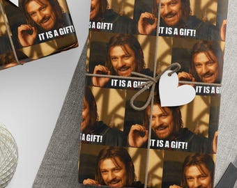 May include: Gift wrapping paper featuring a repeating pattern of a man's face with the text "IT IS A GIFT!". The wrapped gifts are tied with twine and adorned with white tags. A ball of twine and scissors are also visible.