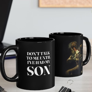 May include: Two black ceramic mugs. One mug has the text "DON'T TALK TO ME UNTIL I'VE HAD MY SON" in white. The other mug features a monster graphic. The mugs are on a light wood surface.