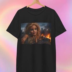 May include: Black t-shirt with a digital art print of a doll with blonde hair and blue eyes, set against a backdrop of fire and a cityscape. The doll is holding a cigarette. The t-shirt is hanging on a wooden hanger.