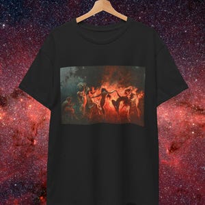 May include: Black t-shirt featuring a rectangular print of a classical painting depicting figures in a fiery, reddish-orange scene. The artwork shows multiple figures in motion, with a dark background. The t-shirt is hanging on a wooden hanger.