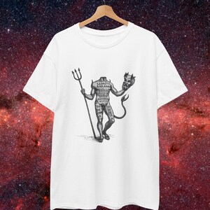 May include: White t-shirt featuring a black and white illustration of a headless figure holding a trident and a devil's head. The figure has text on its torso and a tail. The shirt is hanging on a wooden hanger.