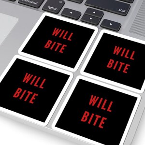 May include: Four square stickers with the text "WILL BITE" in red on a black background. The stickers are placed on a laptop's trackpad. The laptop has a silver body and a black keyboard.