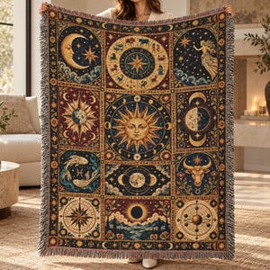 May include: A rectangular woven throw blanket featuring a dark blue and gold celestial design. The pattern includes a central sun, a zodiac wheel, moon phases, stars, and various astrological symbols arranged in a grid of nine distinct panels.
