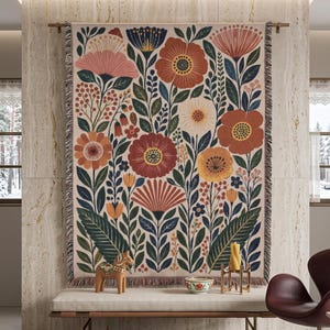 Puede incluir: Un tapiz de pared tejido rectangular que presenta un denso patr&oacute;n bot&aacute;nico de flores y hojas estilizadas en tonos terracota, azul profundo, crema y amarillo mostaza, acabado con un borde de flecos en la parte superior e inferior.