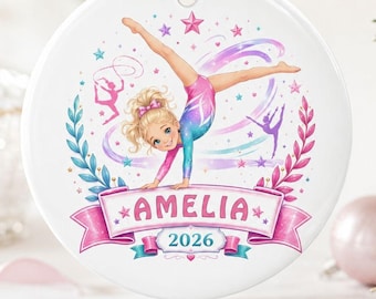 Op de afbeelding: Een rond wit keramieken ornament met een blonde gymnaste in een roze en blauw turnpakje die een handstand maakt. Het ontwerp bevat roze en blauwe lauriertakken, sterren en een banner met de naam AMELIA en het jaartal 2026 erop gedrukt.