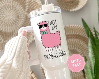 Op de afbeelding: Witte beker met een handvat, versierd met een roze lama met zonnebril en een vlinderdas. De tekst luidt "NOT MY PROB-LLAMA". De beker heeft een wit deksel en een rietje.