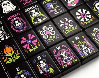 May include: A set of black rectangular mahjong tiles featuring colorful graphic illustrations of bulldogs in various costumes, floral patterns, and seasonal motifs. Each tile displays distinct designs including pumpkins, ghosts, and letters like E, S, W, N, and JOKER, rendered in vibrant neon-toned ink.