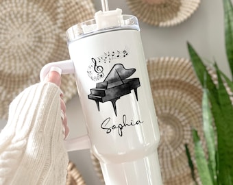 Puede incluir: Vaso térmico blanco con una ilustración de piano en negro y gris, notas musicales y el nombre "Sophia". El vaso tiene un asa blanca y una tapa transparente con pajita.