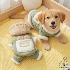 May include: A light olive green quilted dog jacket with white sherpa fleece trim and a hood. The jacket features a white sherpa pocket on the back with the word lucky printed on a rectangular patch and two small rounded ears on the top edge.