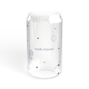 Könnte beinhalten: Ein klares, becherförmiges Trinkglas mit blauen Himmelsmotiven, darunter Herzen, Sterne, eine Sonne und ein Mond. Die Worte "made of peace" sind blau auf dem Glas aufgedruckt. Das Glas ist leer und steht auf weißem Hintergrund.