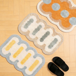 Puede incluir: Una colección de alfombras decorativas en varias formas y colores. Una alfombra es azul claro con rayas amarillas, otra beige con rayas grises y una tercera naranja con lunares grises. También se ven dos zapatillas negras.