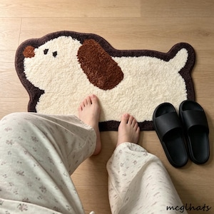 May include: A tufted rug shaped like a dog with a cream-coloured body, a dark brown ear, a dark brown nose, and a dark brown border. The rug features a simple, stylised design of a dog in profile with a small tail and two dark brown eyes.