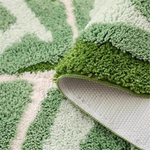 May include: A close-up shot of a green and white patterned bath mat. The mat features a thick, textured pile with a repeating leaf design. The underside is white with a non-slip texture, and the edges are finished with a green border.