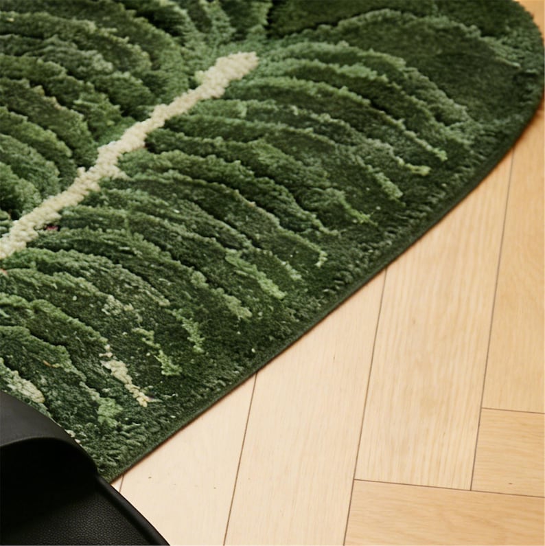 May include: A green leaf-shaped rug with a white vein detail. The rug has a textured, plush surface and is placed on a light-colored wooden floor. The rug's design mimics a tropical leaf.