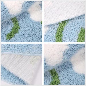 May include: Close-up of a blue bath mat with a floral design. The mat features white flower-shaped accents with green stems and leaves. The backing is white and textured, providing a non-slip surface.