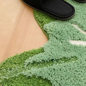 May include: A close-up of a green, textured rug with a leaf-like design. A black slipper rests on the rug. The rug has varying shades of green and a white accent.