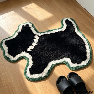 May include: A tufted rug shaped like a dog, featuring a black center, a thick white border, and an outer dark green trim. The rug has a textured, plush surface and is designed in the silhouette of a terrier-style dog with a collar detail.
