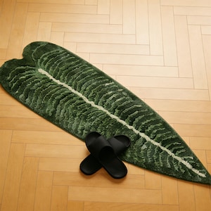 May include: A green leaf-shaped rug with a white central vein and textured details, paired with black sandals. The rug is a vibrant shade of green, and the sandals are black. The rug measures approximately 60 inches long.
