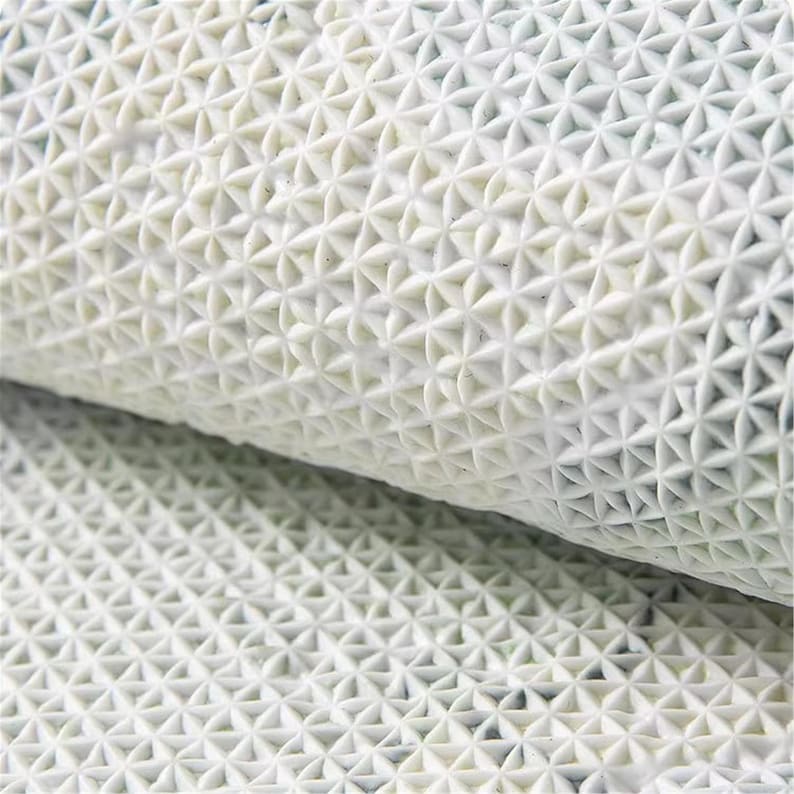 May include: Close-up of a rolled white textured mat. The mat has a repeating pattern of small, raised, star-shaped designs. The texture appears to be made of a flexible material, possibly rubber or a similar substance.