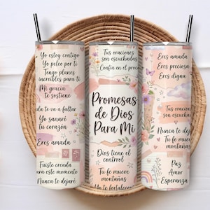 May include: Three cylindrical tumblers with black straws, featuring a pastel-colored design with floral accents, stars, and hearts. The tumblers display Spanish text including phrases like Promesas de Dios Para Mi, Eres amada, and Tu fe mueve montañas.
