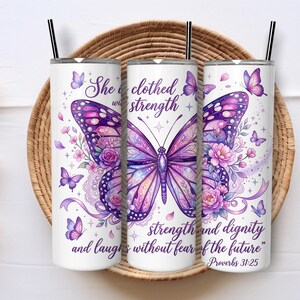 Könnte beinhalten: Ein weißer zylindrischer Becher mit schwarzem Strohhalm, verziert mit einem großen lila Schmetterling, rosa Blumenakzenten und dem Text "She is clothed with strength and dignity and laughs without fear of the future" sowie "Proverbs 31:25".