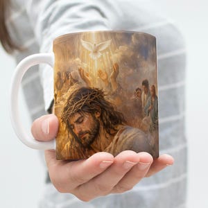 K&ouml;nnte beinhalten: Wei&szlig;e Keramik-Tasse mit religi&ouml;sem Bild. Das Kunstwerk zeigt einen Mann mit einer Dornenkrone, umgeben von Figuren und einer Taube. Die Tasse hat einen wei&szlig;en Henkel und eine gl&auml;nzende Oberfl&auml;che.