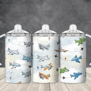 Op de afbeelding: Drie witte tuitbekers met een cartoonvliegtuigpatroon. Het ontwerp toont verschillende vliegtuigen in blauw, groen en oranje, met gestippelde vliegroutes en wolken op een lichtblauwe achtergrond. Elke beker heeft een witte handgreep.