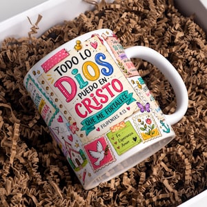 May include: A white ceramic mug featuring a colourful collage of stamps and notes with the Spanish text Todo lo puedo en Cristo que me fortalece Filipenses 4:13, alongside illustrations of a white dove, a church, a butterfly, and floral motifs.