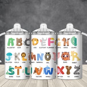 May include: Three white sippy cups with handles, each displaying the alphabet with animal illustrations. The letters are in various colours, with corresponding animals like an alligator, bear, and cat. The cups are designed for toddlers.