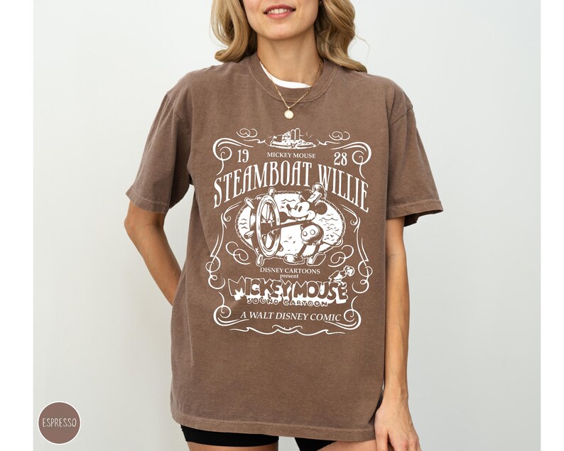 May include: Espresso-colored t-shirt featuring a vintage design with the text "Steamboat Willie" and "Mickey Mouse." The graphic includes an image of Mickey Mouse at the helm of a steamboat. The shirt is a relaxed fit.