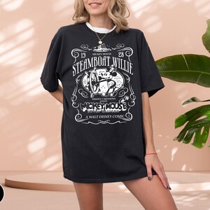 May include: Black t-shirt featuring a vintage Steamboat Willie design. The graphic includes the text "19 Steamboat Willie 28" and "Mickey Mouse" with a cartoon image of Mickey Mouse. The shirt is a classic Disney cartoon design.