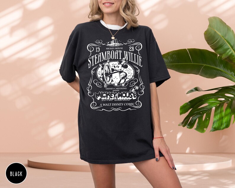 May include: Black t-shirt featuring a vintage Steamboat Willie design. The graphic includes the text "19 Steamboat Willie 28" and "Mickey Mouse" with a cartoon image of Mickey Mouse. The shirt is a classic Disney cartoon design.