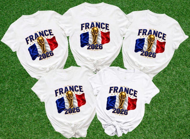 May include: Five white t-shirts featuring a graphic print with the word FRANCE in blue, a gold trophy, the French flag in blue, white, and red, and the year 2026 in blue. Each shirt has a round neckline and short sleeves with a knotted hem detail.